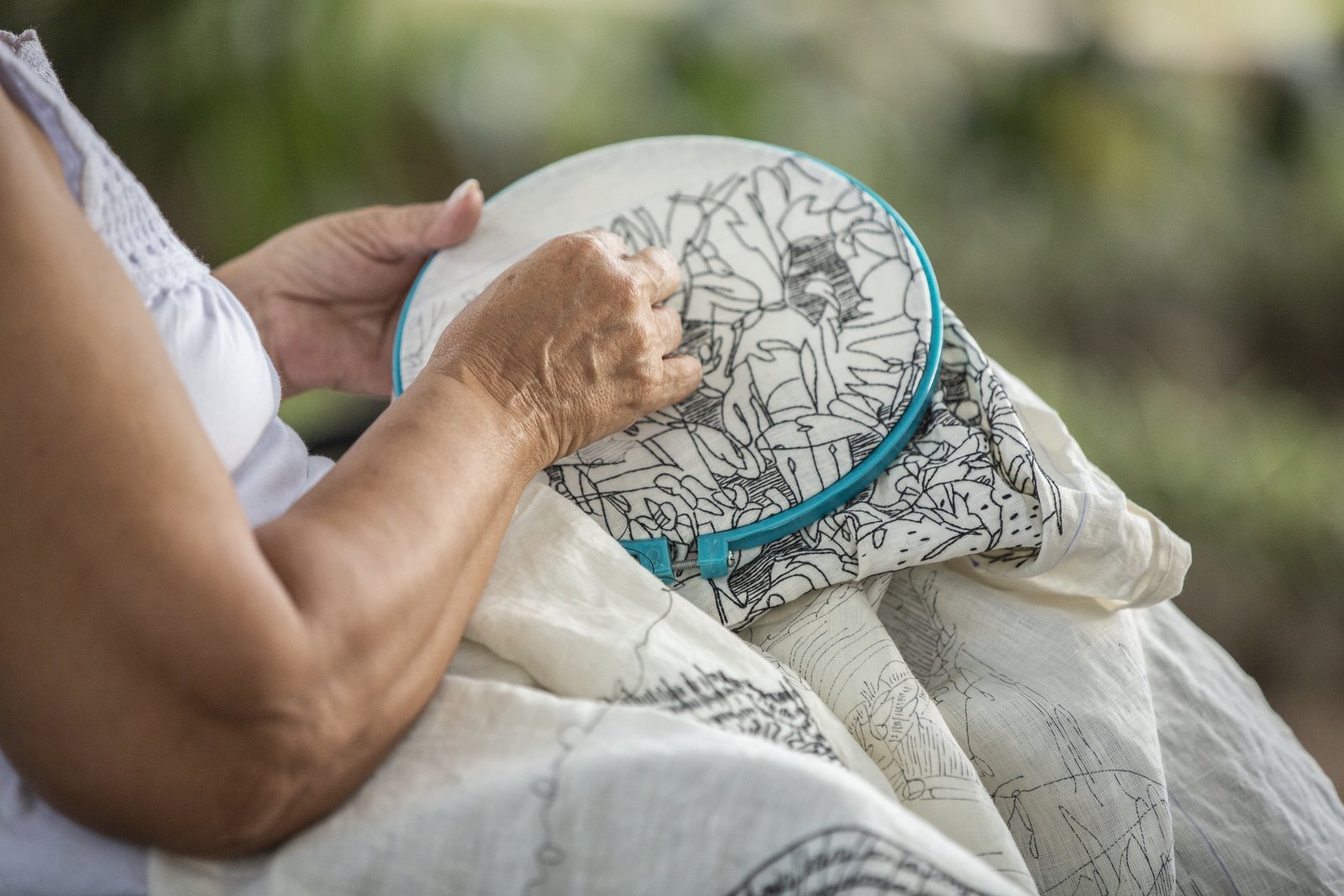 Hands guiding a hoop through a length of embroidered linen, outdoors