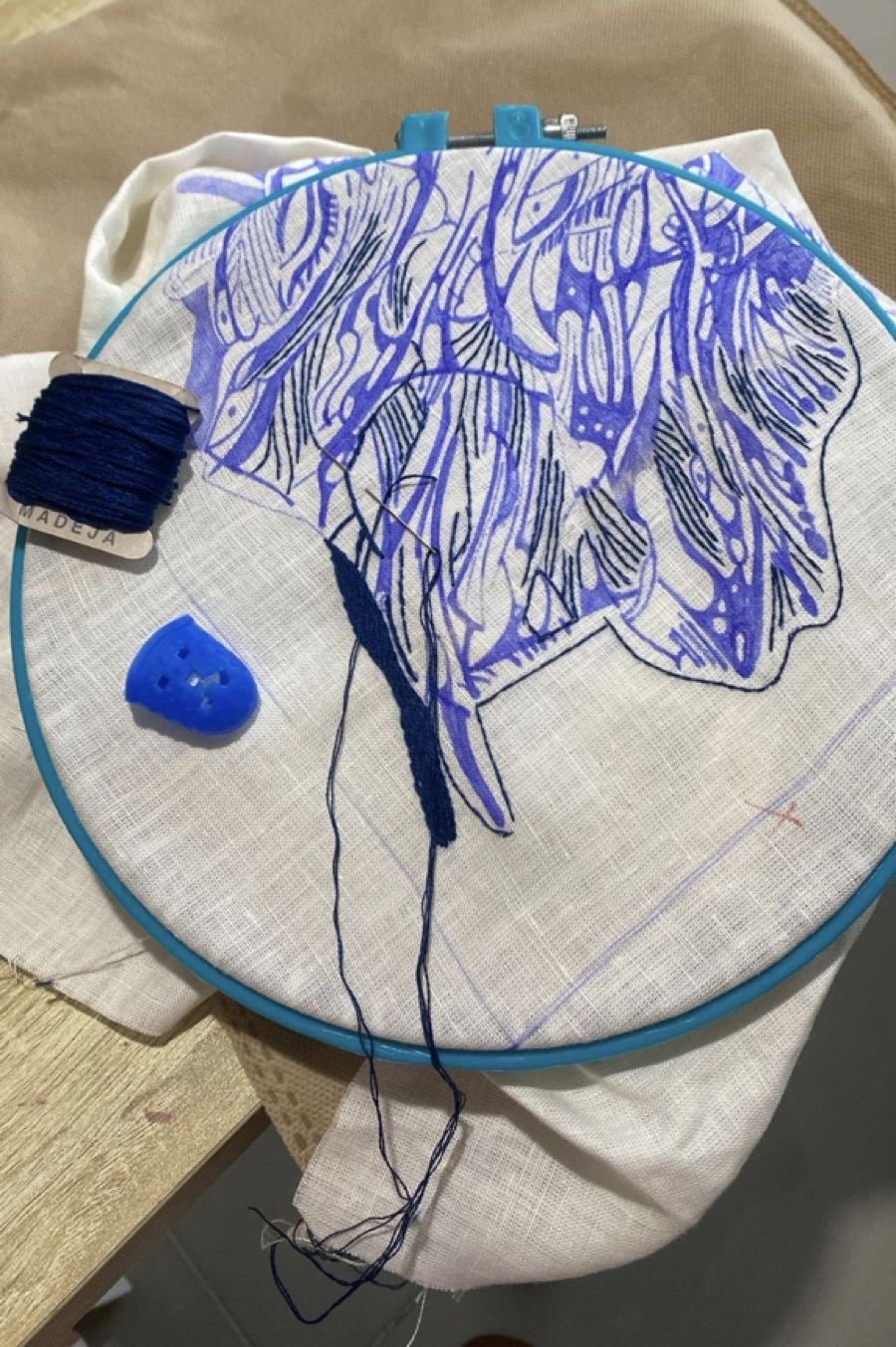 Hoop with blue-marker sketch, thread spool and button beside it
